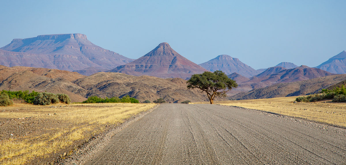 Schotterpiste von Namibias Torra Conservancy mit Akazie und Tafelbergen