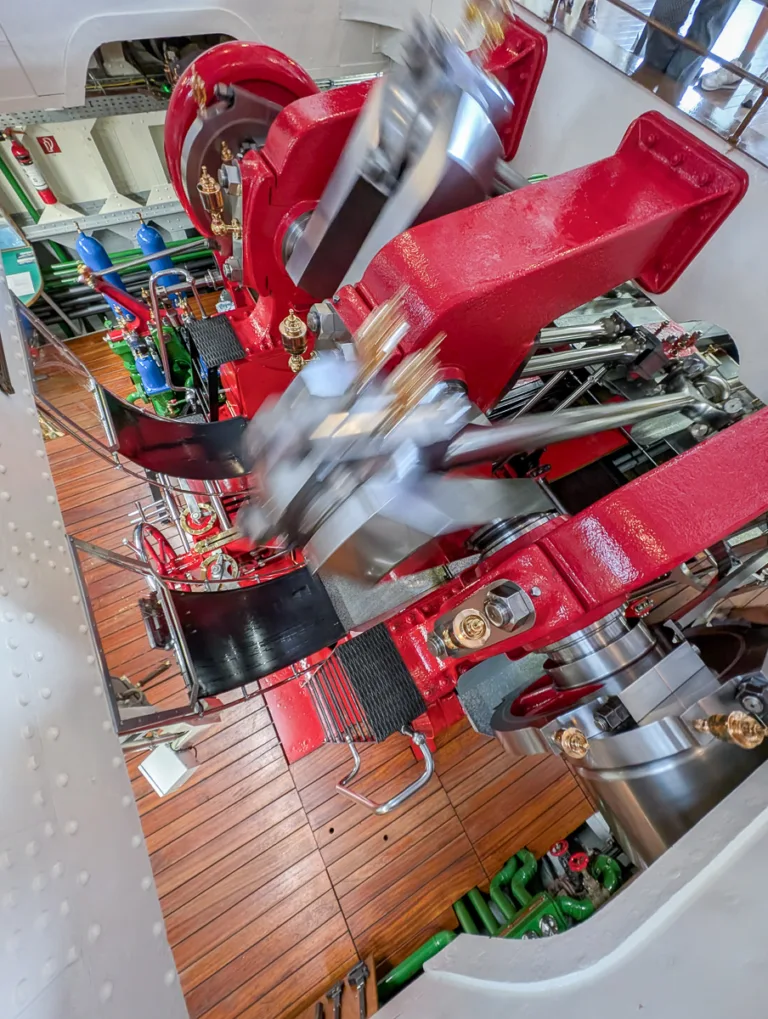 Blick in den laufenden Maschinenraum eines rot lackierten Schaufelraddampfers mit Holzboden