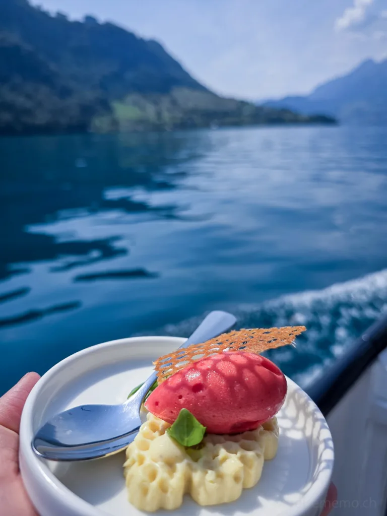 Kleine Dessert-Kreation mit Beerensorbet und Waffel auf einem Teller, im Hintergrund ein See und Berge