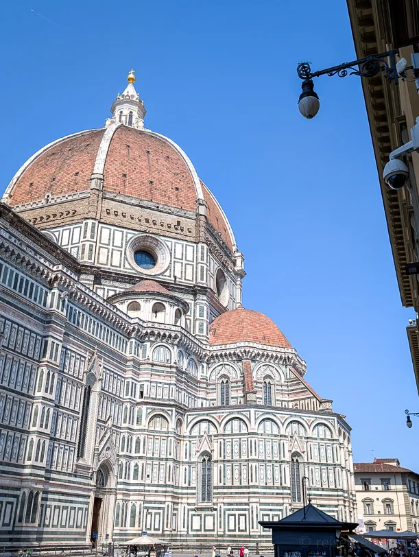 Nahaufnahme der rotbraunen Ziegelkuppel des Doms Santa Maria del Fiore in Florenz mit der charakteristischen grün-weiss-rosa Marmorfassade vor strahlend blauem Himmel