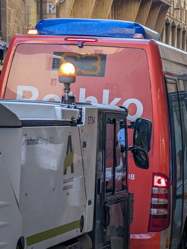 Ein weisses Strassenreinigungsfahrzeug der Firma Alia Servizi Ambientali steht hinter einem roten Linienbus mit der Aufschrift Rothko in Florence in einer engen Florentiner Gasse