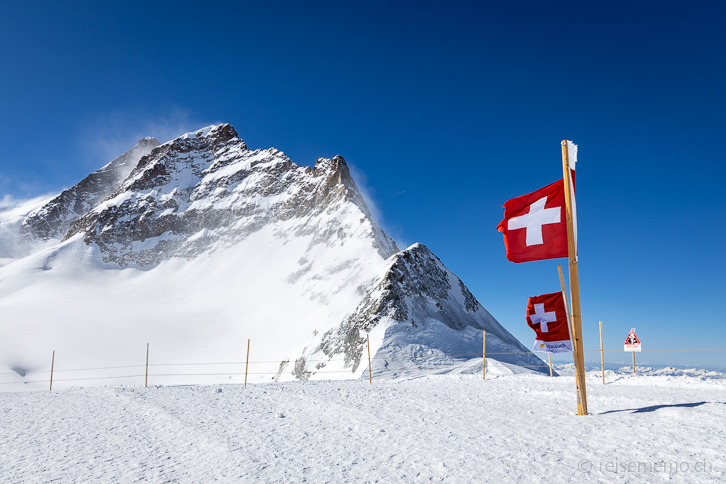 Windiges Jungfraujoch mit Schweizer Fahnen und Jungfrau und Mathildespitze