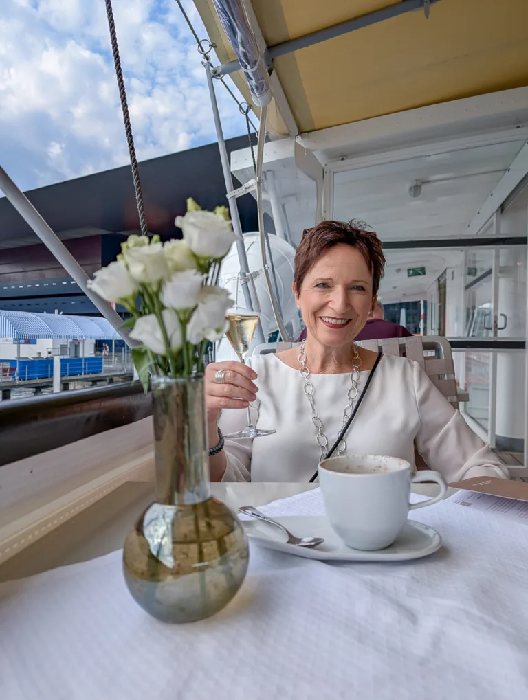 Frau sitzt an gedecktem Tisch mit Kaffee und Blumen auf einem Dampfschiff auf dem Vierwaldstättersee bei Luzern