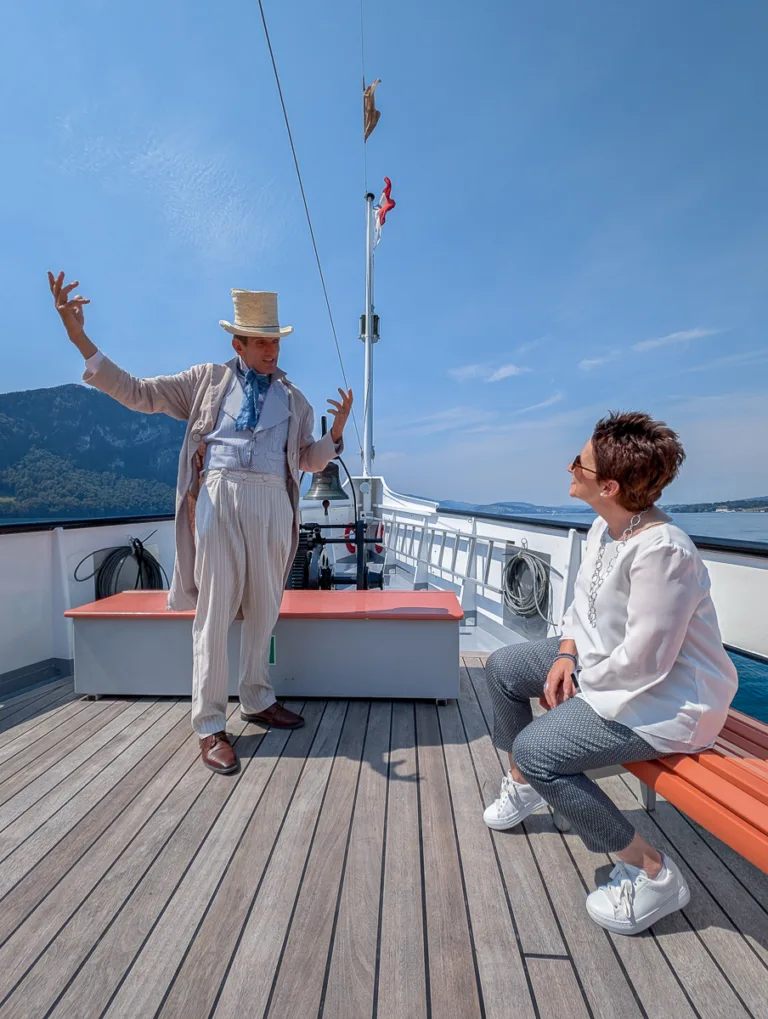 Schauspieler in historischer Kleidung erzählt einer Frau auf dem offenen Deck eines Dampfschiffs am Vierwaldstättersee eine Geschichte