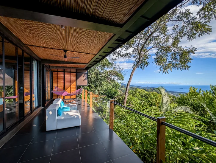 Überdachte Hotelterrasse des Kura Boutique Hotels mit weissen Möbeln und Panoramablick über tropischen Regenwald zum Pazifischen Ozean.