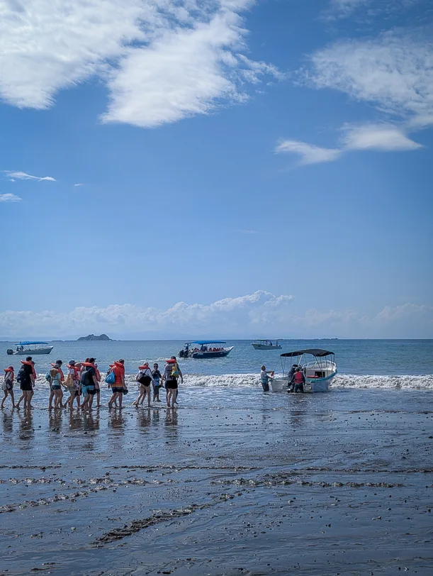 Touristen steigen bei Ebbe am Strand von Uvita in ein Boot für eine Walbeobachtungstour im Nationalpark Marino Ballena