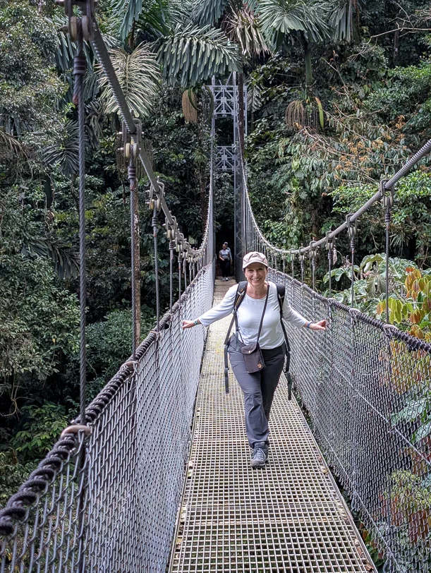 Wanderin überquert eine Metallhängebrücke zwischen hohen Bäumen im tropischen Regenwald