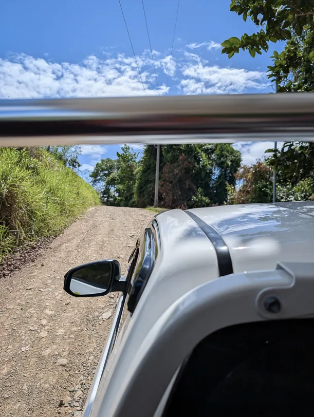 Silbernes Auto auf unbefestigter Schotterpiste umgeben von dichtem grünem Tropenwald unter blauem Himmel mit weissen Wolken