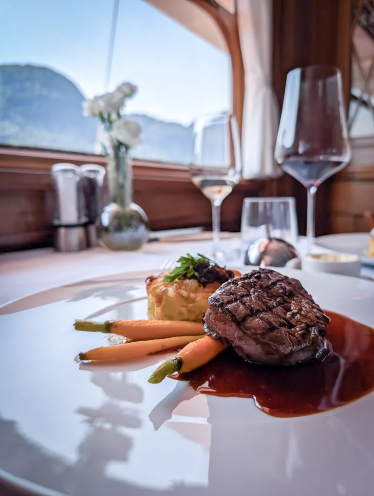 Edles Gourmetgericht mit Gemüse und Fleisch auf weissem Teller, im Hintergrund Fenster mit Blick auf Berge