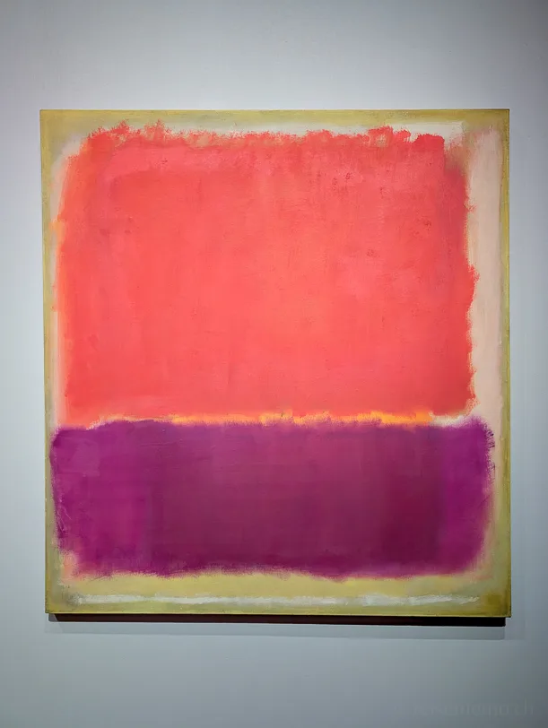 "Orange and Tan, 1954" Abstraktes Gemälde von Mark Rothko mit einem grossen orangeroten Farbfeld oben und einem violetten Farbfeld unten, getrennt durch einen schmalen gelblichen Streifen, an einer weissen Galeriewand