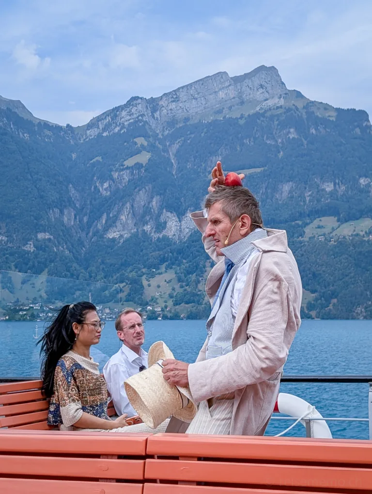 Person in ausgefallenem Kostüm steht auf einem Schiff mit Blick auf den Vierwaldstättersee und umliegende Berge